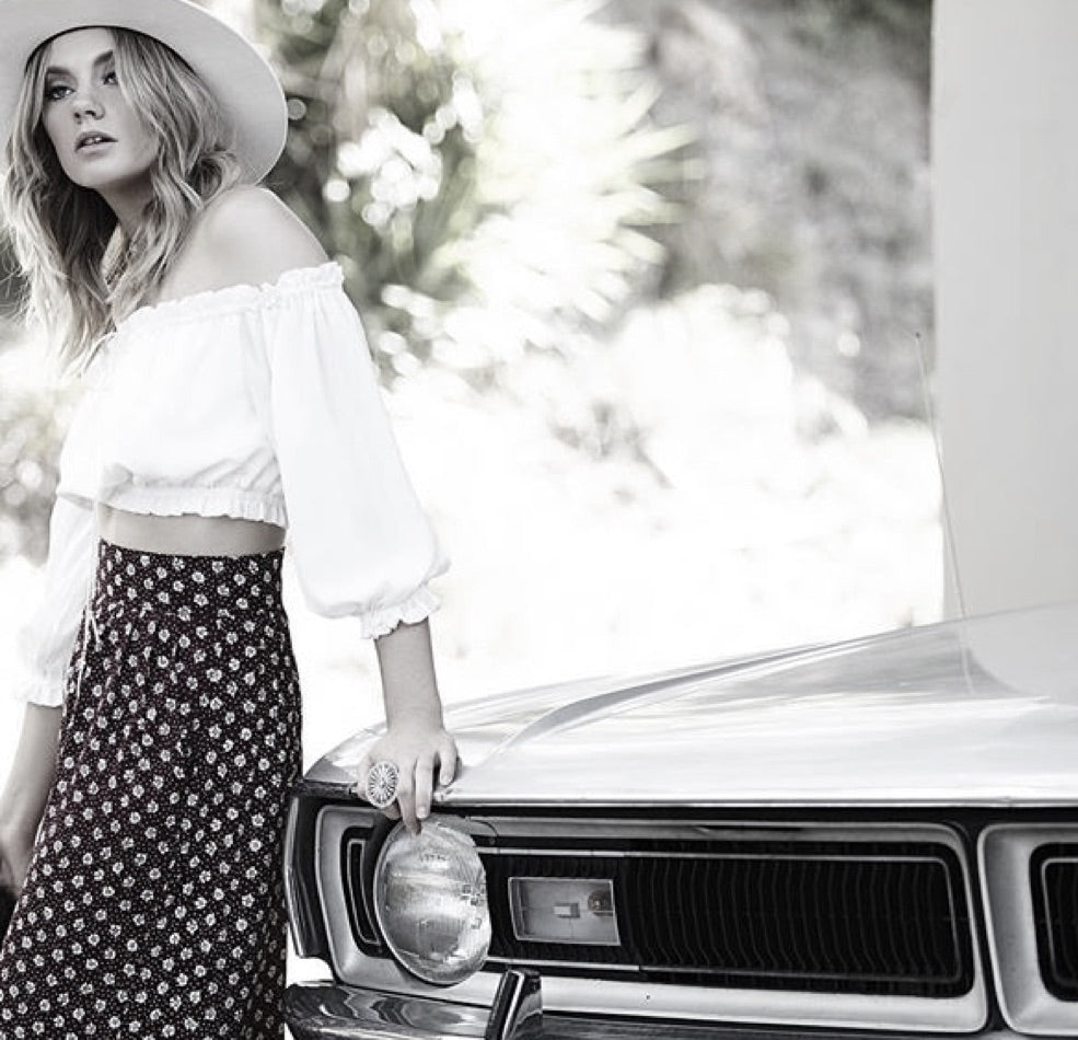 Black and white photo of a blonde lady standing in front of a vintage car wearing essentials ivory wool felt hat