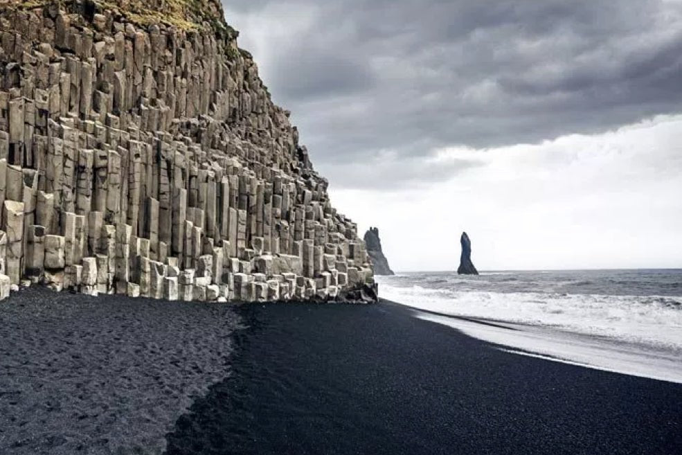 Grey piller rock on a black sand beach with waves crashing