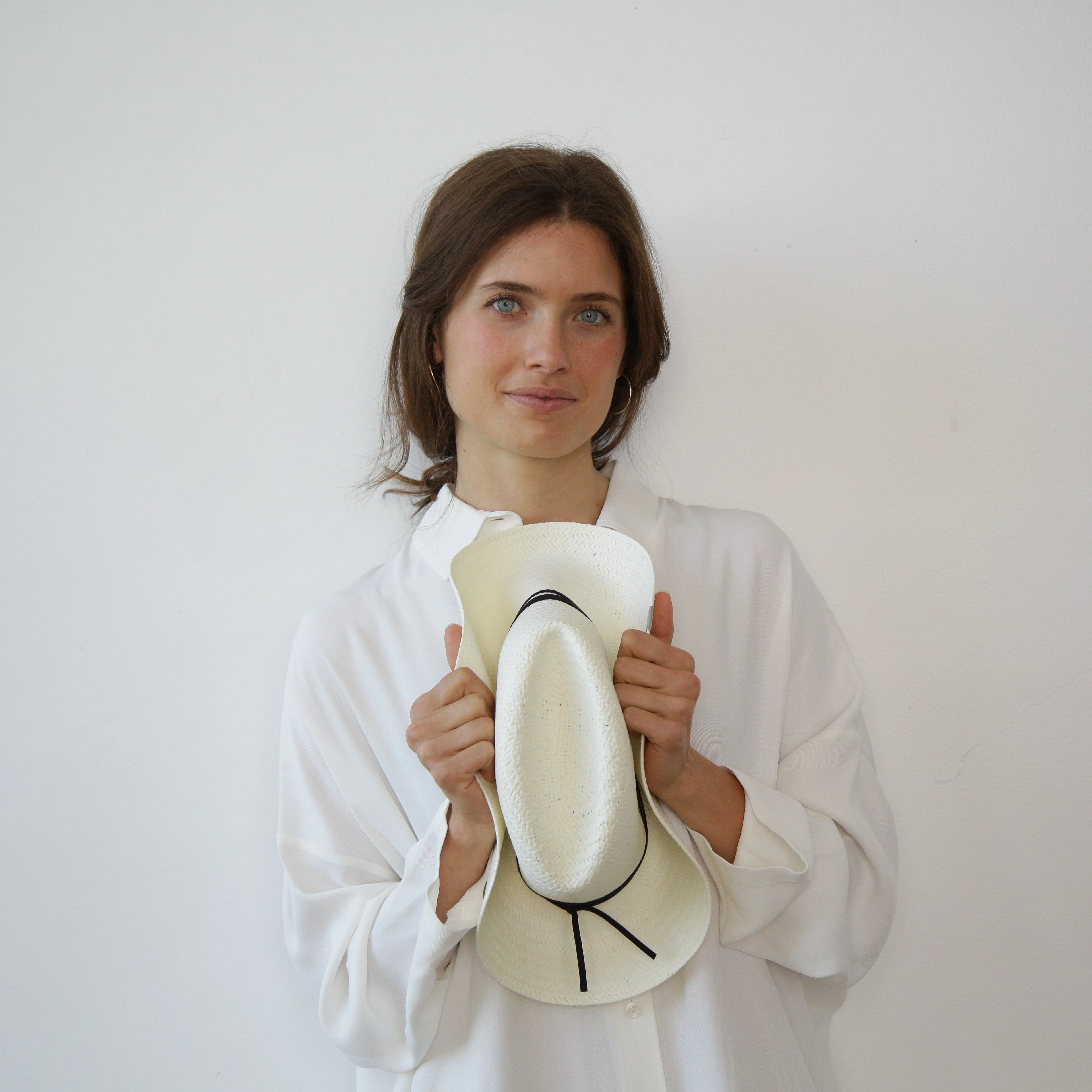 Woman holding a white hat with black details against a plain background